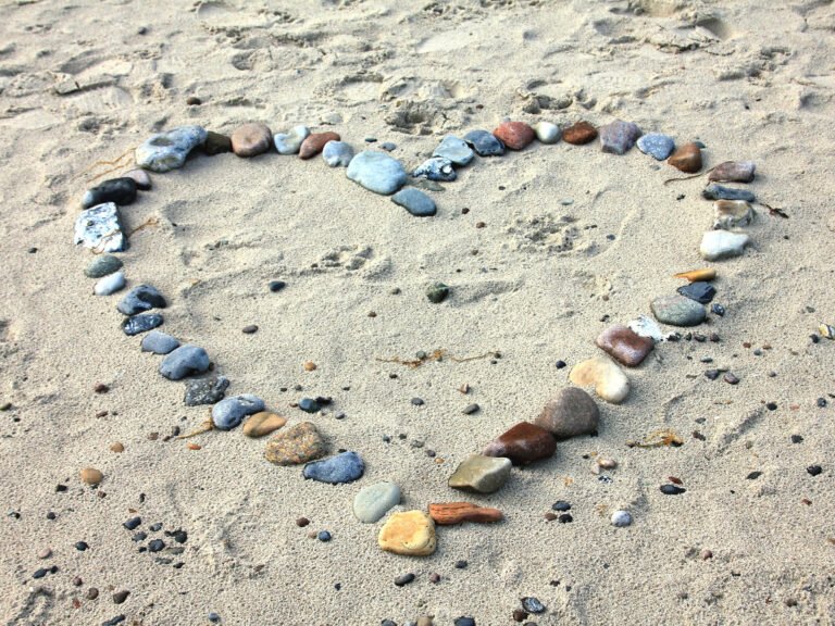 Ein Herz aus bunten kleinen Steinen auf Sand am Strand