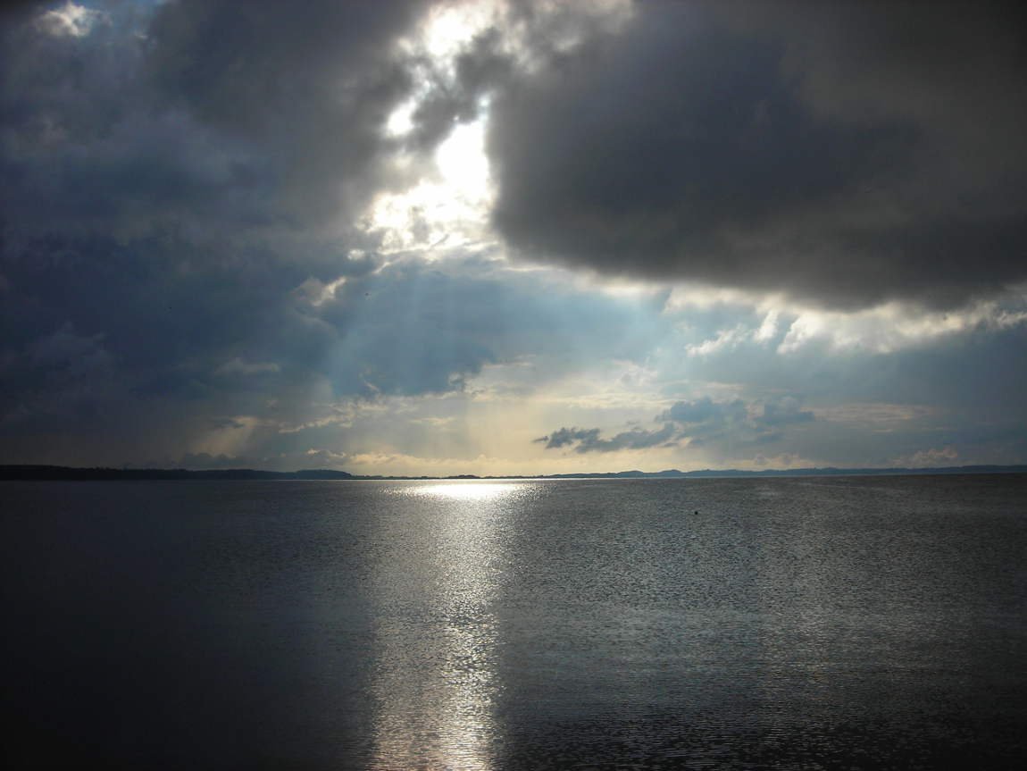 aus dunklen Wolken fällt ein Lichtkegel auf die gekräuselte Wasseroberfläche der Ostsee