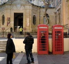 Zwei rote Telefonzellen auf Malta und zwei durkel gekleidete Personen