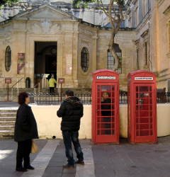 Zwei rote Telefonzellen auf Malta und zwei durkel gekleidete Personen